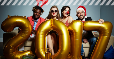 Vier Leute in Kostümen, die auf dem Sofa sitzen und eine goldene 2017 halten
