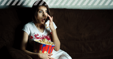 Junge Frau sitzt mit Popcorn vorm TV und schaut Horrorfilme