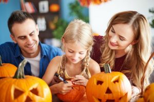Familie beim Halloween Kürbis schnitzen - Mädchen malt Gesicht auf Kürbis