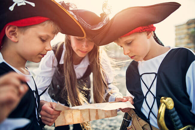 Drei Kinder in Piratenkostümen lesen Schatzkarte
