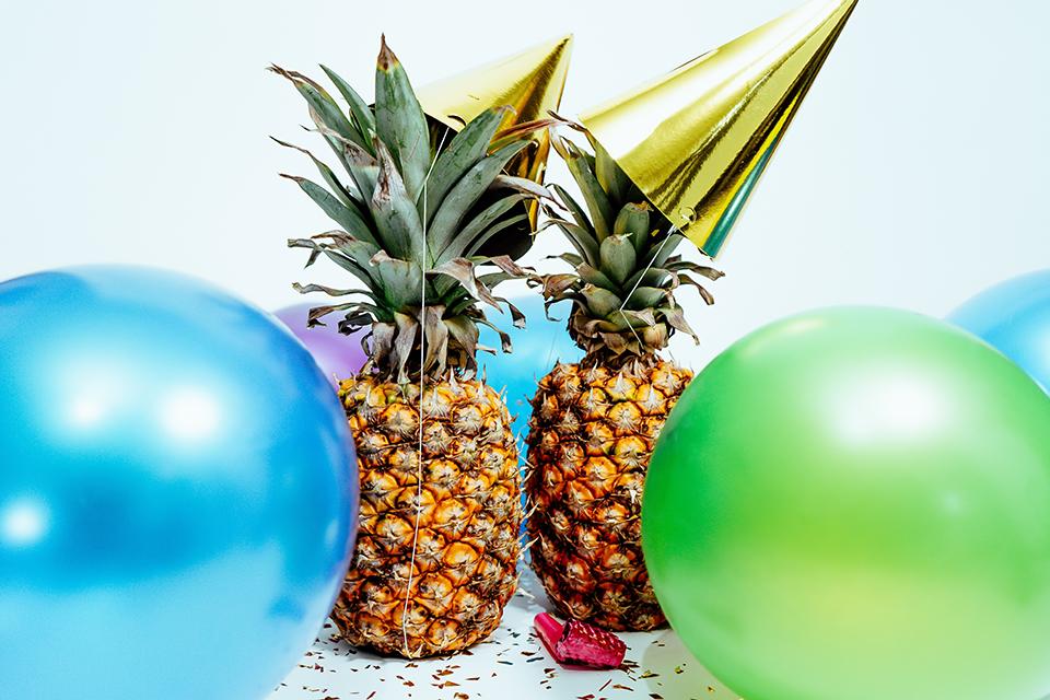Ananas mit Partyhüten und Luftballons